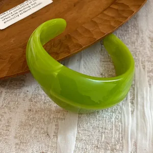 Dettaglio di un bracciale rigido aperto in acrilico verde lime su vassoio in legno