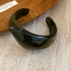 Primo piano di un bracciale aperto in acrilico verde scuro con trama marmorizzata