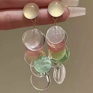 Primer plano detallado de pendientes de borlas de concha con discos translúcidos
