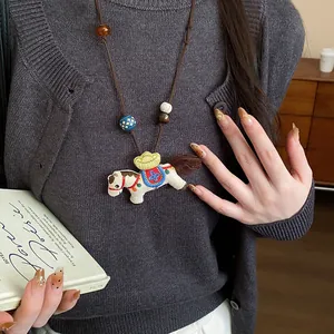 Macro view of a handmade embroidered horse pendant necklace on a dark grey knit sweater
