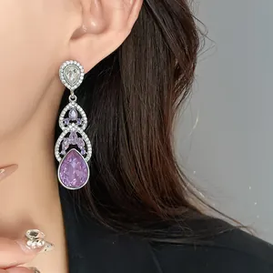 Macro detail of elegant long teardrop earrings featuring purple crystals and rhinestones.
