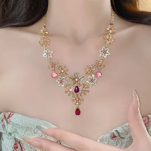Detailed view of a vintage gold necklace with rhinestone flowers and red teardrop gems.