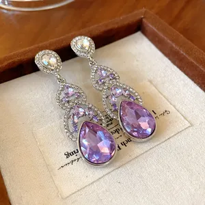Close-up detail showing sparkling purple teardrop crystal dangle earrings with silver needle.