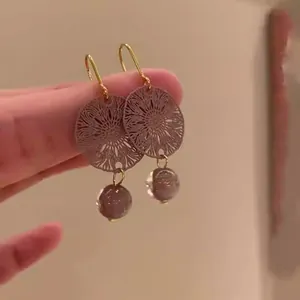 Detalle de pendientes elegantes con disco calado metálico y cuentas de color púrpura