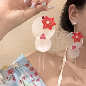 Primer plano de pendientes de borla de concha con encaje rojo y perla en modelo.