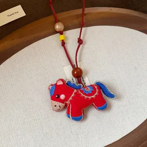 Close-up of embroidered red horse pendant with wooden and resin beads on red cord
