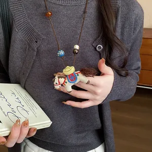 Close-up of a handmade fabric horse necklace with wooden beads on a knitted sweater.
