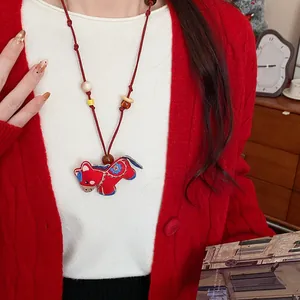 Detailed shot of an embroidered red horse pendant necklace worn with a red cardigan