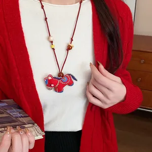 Detailed view of an embroidered red horse necklace with wooden beads on a red knit