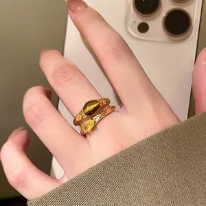 Close-up of 18k gold plated open rings with tiger eye stone and zircon on finger.