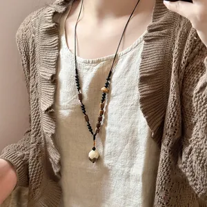 Close-up of ethnic style long necklace with pine nut pendant on a knitted sweater.