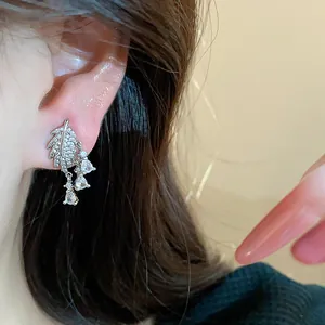 Dettaglio di un orecchino a foglia placcato oro 18k con zirconi pendenti su un orecchio.