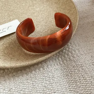 Elegante brazalete abierto de acrílico jaspeado ámbar con textura de diseño ondulado.