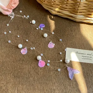 Detailed view of an iridescent mermaid tail and shell charm necklace with white pearls