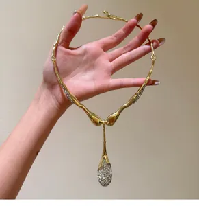 Primo piano di una collana dorata con pendente a goccia irregolare e strass luccicanti.