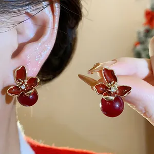 Primer plano de pendientes de flores de esmalte rojo con perla roja en la oreja.
