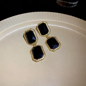 Vintage geometric black crystal earrings with textured gold frame on a ceramic plate