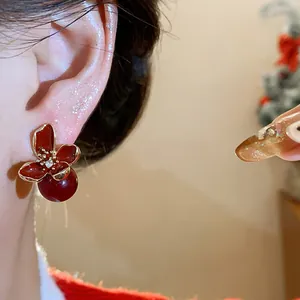 Primer plano de elegantes pendientes de flor de esmalte rojo con gota de perla