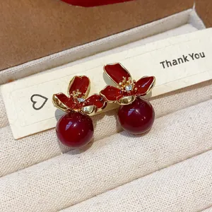 Detalle de pendientes de flor esmaltada roja con perla roja brillante y borde dorado.