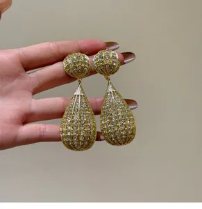 Eleganti orecchini a goccia dorati con strass luccicanti in vista di dettaglio.
