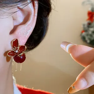 Vista detallada de un exquisito pendiente de flor roja con perla usado en la oreja.