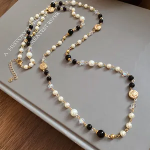 Close-up of long vintage necklace with white pearls, black beads, and gold floral charms.
