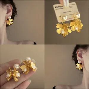 Detailansichten französischer Vintage-Goldblumenohrringe mit Perlen am Modell und auf Produktkarte.