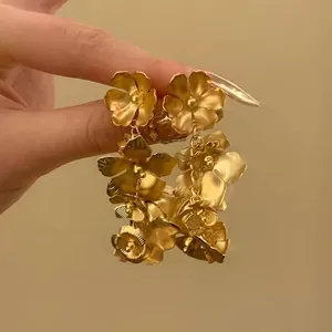 Nahaufnahme eleganter goldener Blumenohrringe im französischen Stil zwischen Fingern
