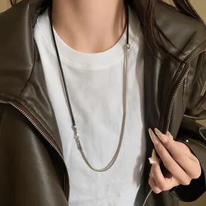 Detail view of a punk style leather cord and metallic snake chain necklace on a model.