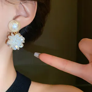 Primer plano de elegantes pendientes de flores blancas con una perla crema en la oreja.