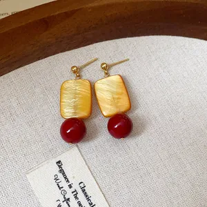 Close-up of vintage drop earrings featuring a yellow rectangle and a red bead detail