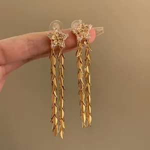 Dettaglio di eleganti orecchini a stella dorati con lunghe nappe di foglie lucide