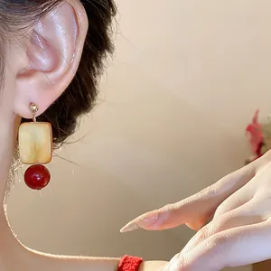 Close-up of retro square glass bead earrings with a red pendant on the model's ear