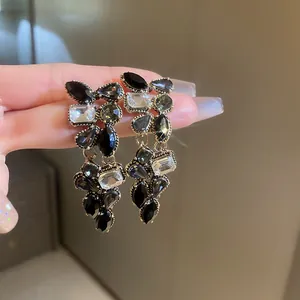Dettaglio di eleganti orecchini pendenti dorati con pietre di cristallo nere e trasparenti.