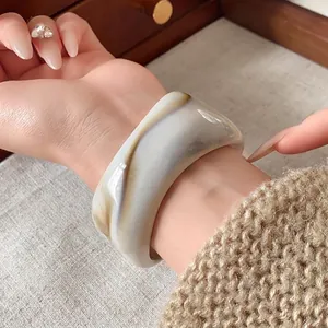 Bracciale rigido largo in resina con trama marmorea irregolare su polso femminile
