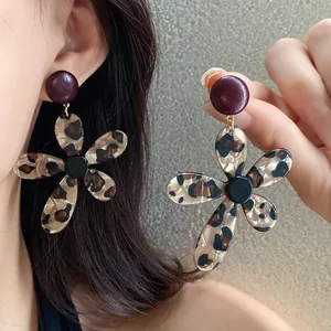 Close-up of leopard print resin flower earrings with silver needles shown worn and held.