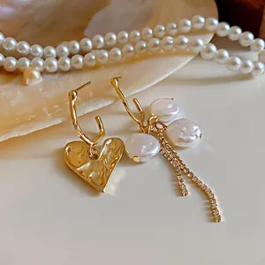 Close-up detail of asymmetric earrings with gold heart and baroque pearl fringe design