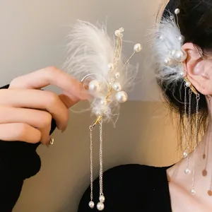 Detalle de un ear cuff de plumas blancas con perlas y borlas largas de metal.
