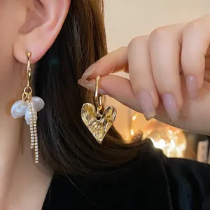 Detailed shot of asymmetric gold heart earrings with pearls and rhinestone tassels