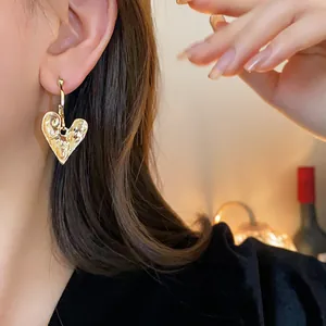 Close-up detail shot of a vintage-style hammered gold heart earring worn on a model.