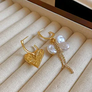 Close-up detail of asymmetrical heart and baroque pearl tassel earrings in a jewelry tray