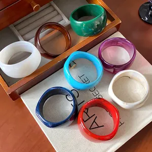 Varietà di bracciali rigidi in resina larghi e irregolari in vari colori su sacchetto lino