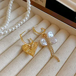 Close-up of asymmetric gold heart and baroque pearl earrings with tassels