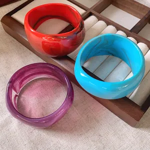 Dettaglio di ampi bracciali in resina irregolari con trama marmorizzata in rosso, blu e viola.