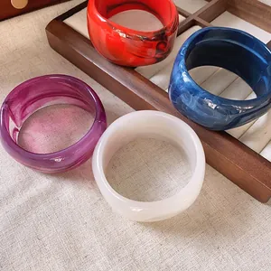 Dettaglio di quattro bracciali rigidi in acrilico marmorizzato su vassoio.