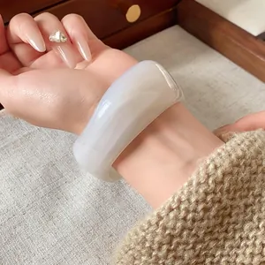 Primo piano di un ampio bracciale irregolare in resina con trama marmorea bianco latte
