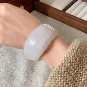 Vista dettagliata di un bracciale rigido largo e irregolare in bianco marmorizzato traslucido.