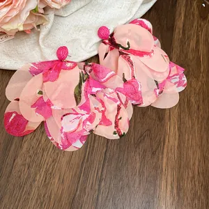 Detail shot of oversized pink floral chiffon petal earrings on a wooden background