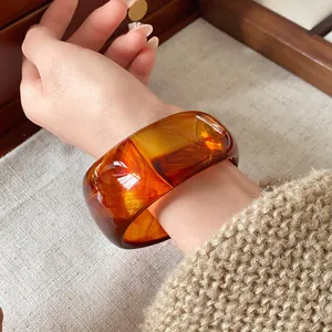 Primo piano di un ampio bracciale irregolare in resina ambrata al polso che mostra la trama
