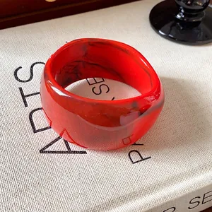 Dettaglio di un bracciale rigido irregolare in resina marmorizzata rossa e venature nere.